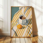 A framed illustration of a cup of coffee, a lemon slice, and a striped cloth on a wooden floor.