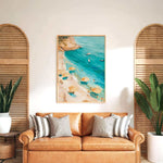 a cozy living room with a large painting of a beach scene hanging on the wall above a brown leather couch. The painting depicts a beach with people enjoying the sun and the sea, surrounded by umbrellas and palm trees. The room is decorated with potted plants and wooden shutters, creating a warm and inviting atmosphere.
