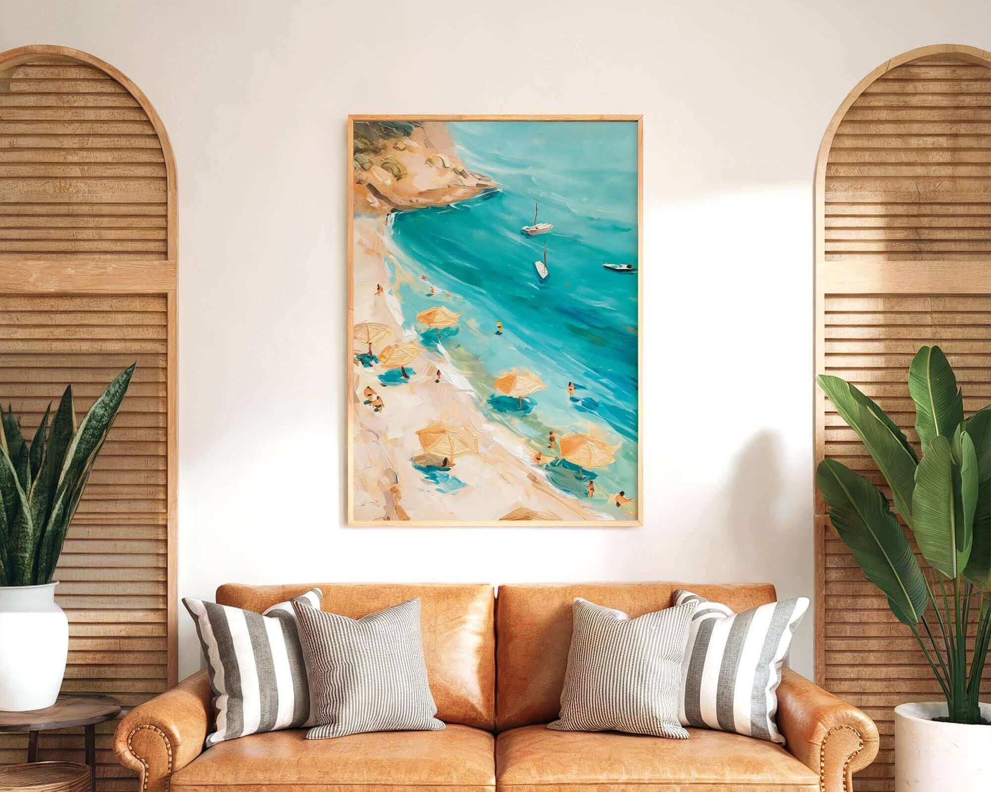 a cozy living room with a large painting of a beach scene hanging on the wall above a brown leather couch. The painting depicts a beach with people enjoying the sun and the sea, surrounded by umbrellas and palm trees. The room is decorated with potted plants and wooden shutters, creating a warm and inviting atmosphere.