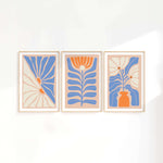 three paintings of blue and orange flowers on a white wall