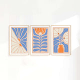 three paintings of blue and orange flowers on a white wall