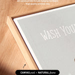 a close-up view of a wooden surface with a framed piece of artwork featuring the phrase "WASH YOURS" in bold white letters.