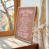 A framed sign on a window sill that reads "LAKESHOUSE RULES" and provides a list of activities to enjoy while at the lake, including "WAKE UP LATE", "GO JUMP IN THE LAST", "SINK IN THE SUN", "TAKE A NAP", "SIP A DRINK", "FEEL THE BREZE", "ENJOY EVERY SUNSET", and "MAKE MEMORIES".