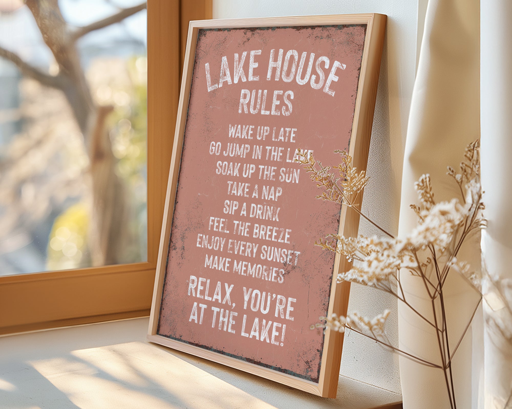 A framed sign on a window sill that reads "LAKESHOUSE RULES" and provides a list of activities to enjoy while at the lake, including "WAKE UP LATE", "GO JUMP IN THE LAST", "SINK IN THE SUN", "TAKE A NAP", "SIP A DRINK", "FEEL THE BREZE", "ENJOY EVERY SUNSET", and "MAKE MEMORIES".