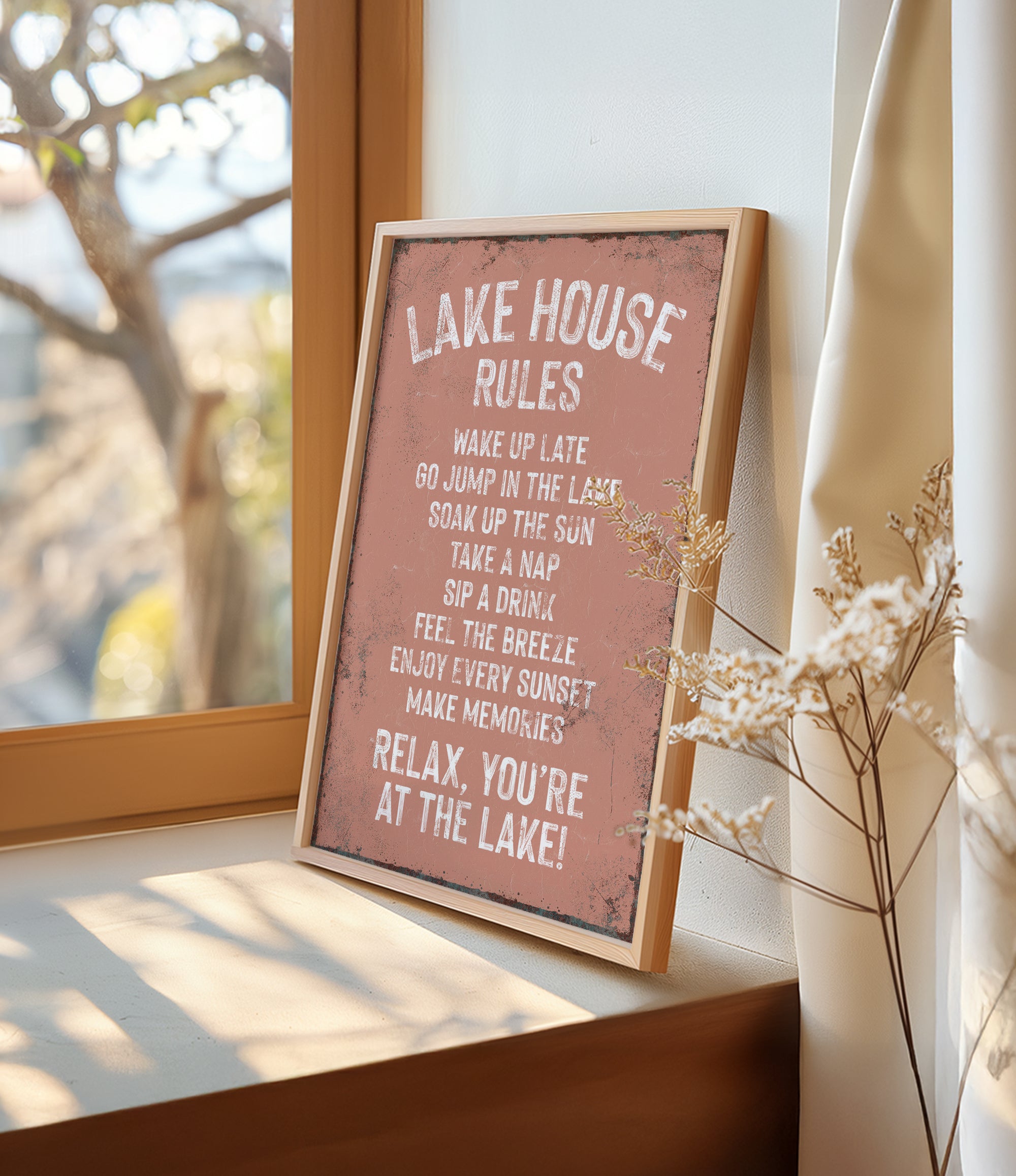A framed sign on a window sill that reads "LAKESHOUSE RULES" and provides a list of activities to enjoy while at the lake, including "WAKE UP LATE", "GO JUMP IN THE LAST", "SINK IN THE SUN", "TAKE A NAP", "SIP A DRINK", "FEEL THE BREZE", "ENJOY EVERY SUNSET", and "MAKE MEMORIES".