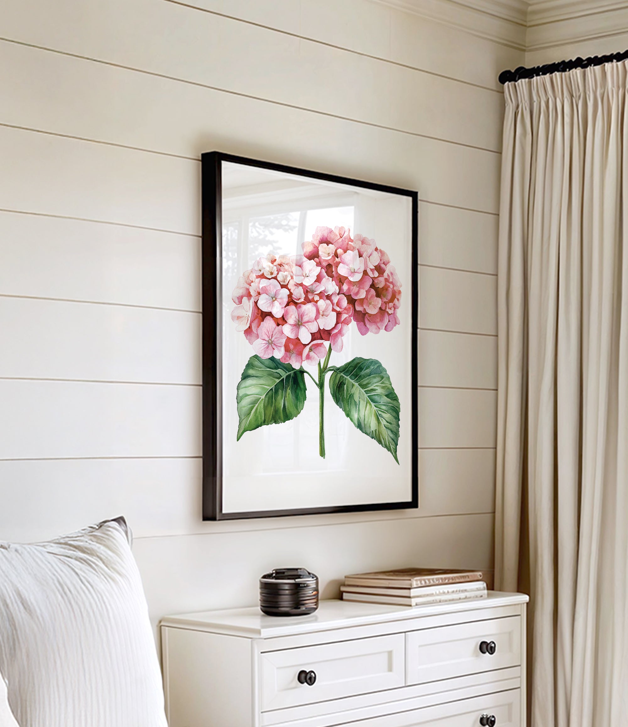 a framed painting of pink hydrangeas hanging on a white wall above a white dresser with a stack of books on top.