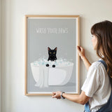 A framed poster with a black cat sitting in a white bathtub filled with bubbles, with the text "WASH YOUR PAWS" displayed above it.