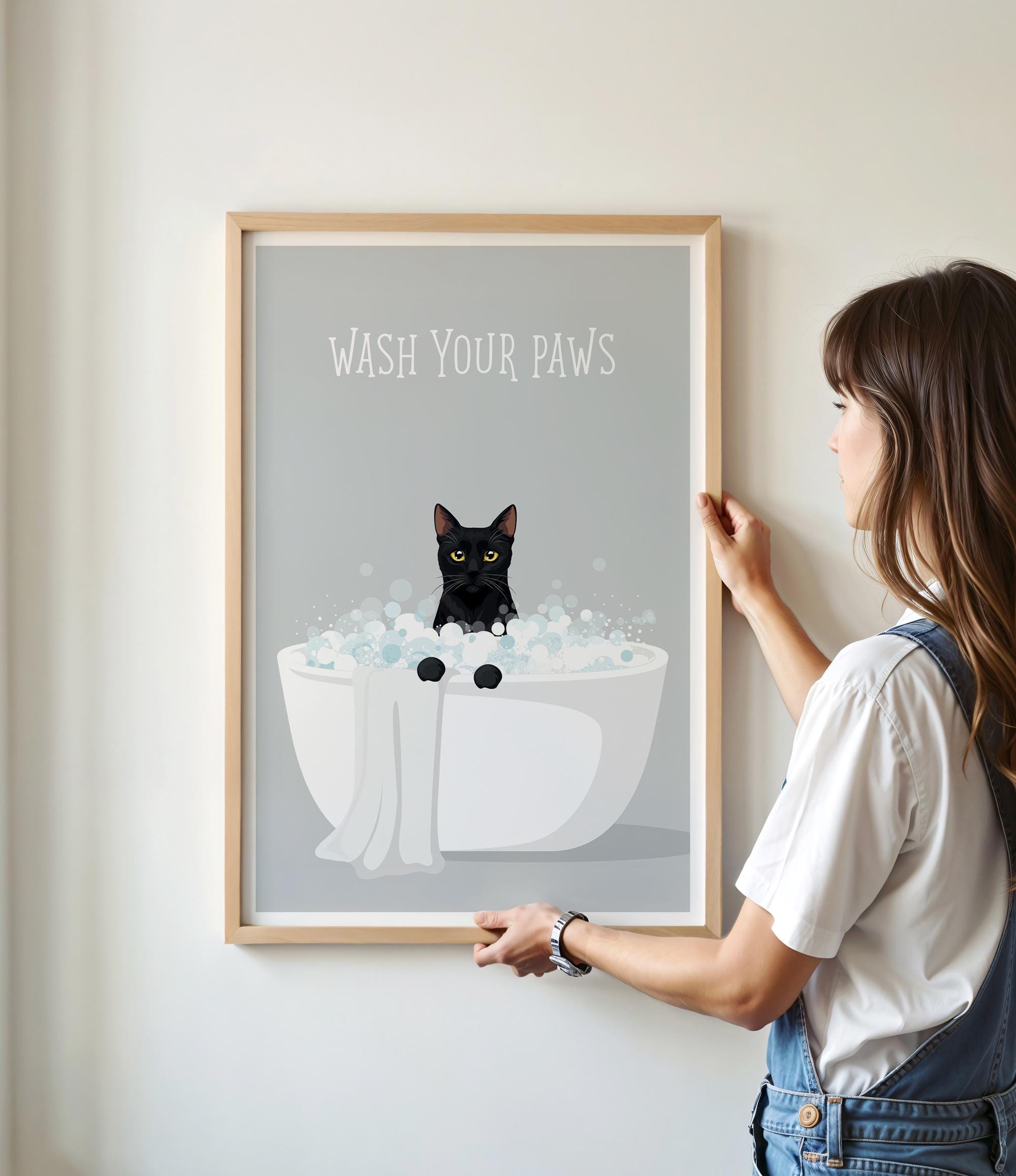 A framed poster with a black cat sitting in a white bathtub filled with bubbles, with the text "WASH YOUR PAWS" displayed above it.