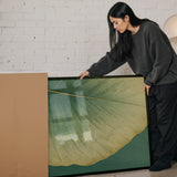 A woman in a gray sweater is leaning over a large framed picture, examining it closely.