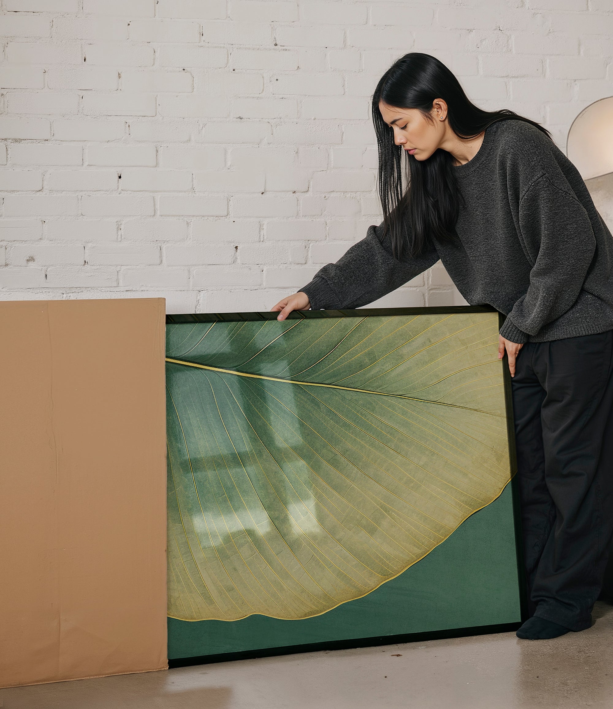 A woman in a gray sweater is leaning over a large framed picture, examining it closely.