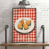 A framed illustration of a plate with three pears is displayed on a wooden shelf against a white brick wall.