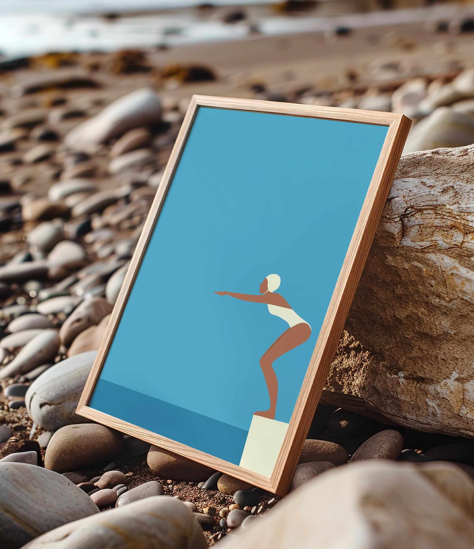 A framed illustration of a woman in a white swimsuit diving off a cliff, set against a blue background, is displayed on a rocky beach.