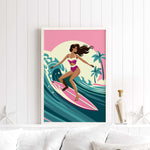A framed illustration of a woman surfing on a pink surfboard against a tropical background.