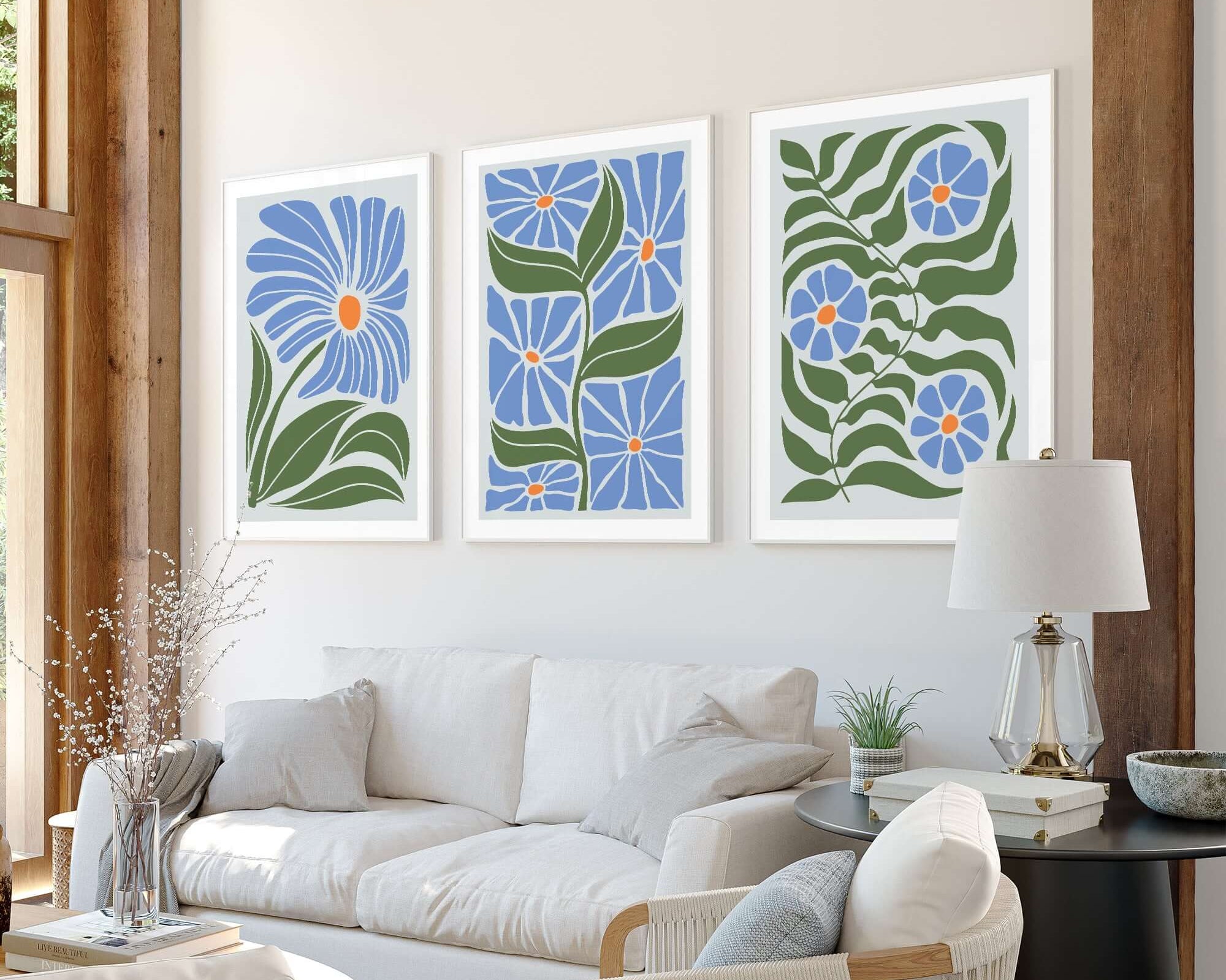 A bright living room with a white sofa, wooden beams, and the Flower Blocks Triptych | Set of Three Prints | 011 of blue floral wall art enhances the home decor.