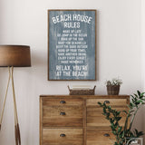 A Beach House Rules Sign in painted wood, harbor blue, hangs above a wooden dresser with a plant and basket, bringing cozy beach house decor to the room.