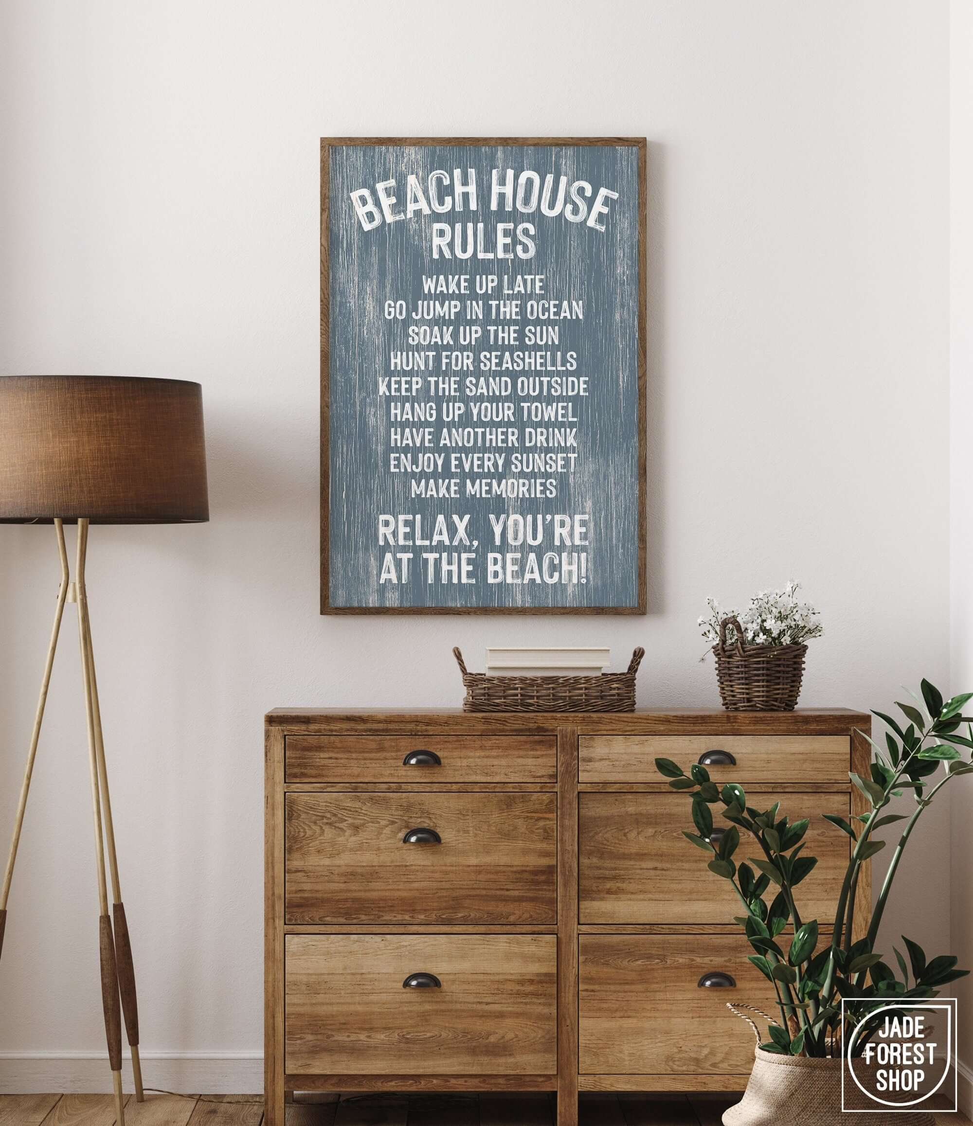 A Beach House Rules Sign in painted wood, harbor blue, hangs above a wooden dresser with a plant and basket, bringing cozy beach house decor to the room.