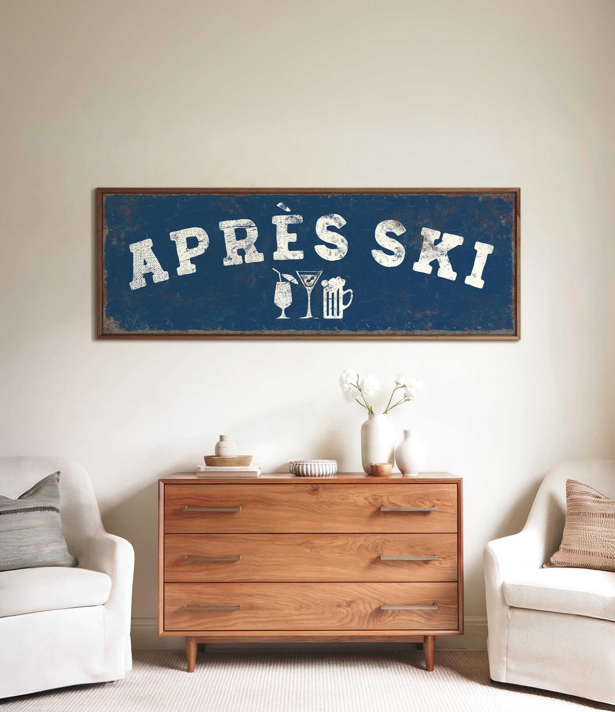 a living room with a large blue sign that says "APRÈS SKI" above a wooden dresser. The dresser has a vase of flowers and a book on it. There are two white chairs in the room, and a small table with a lamp on it.