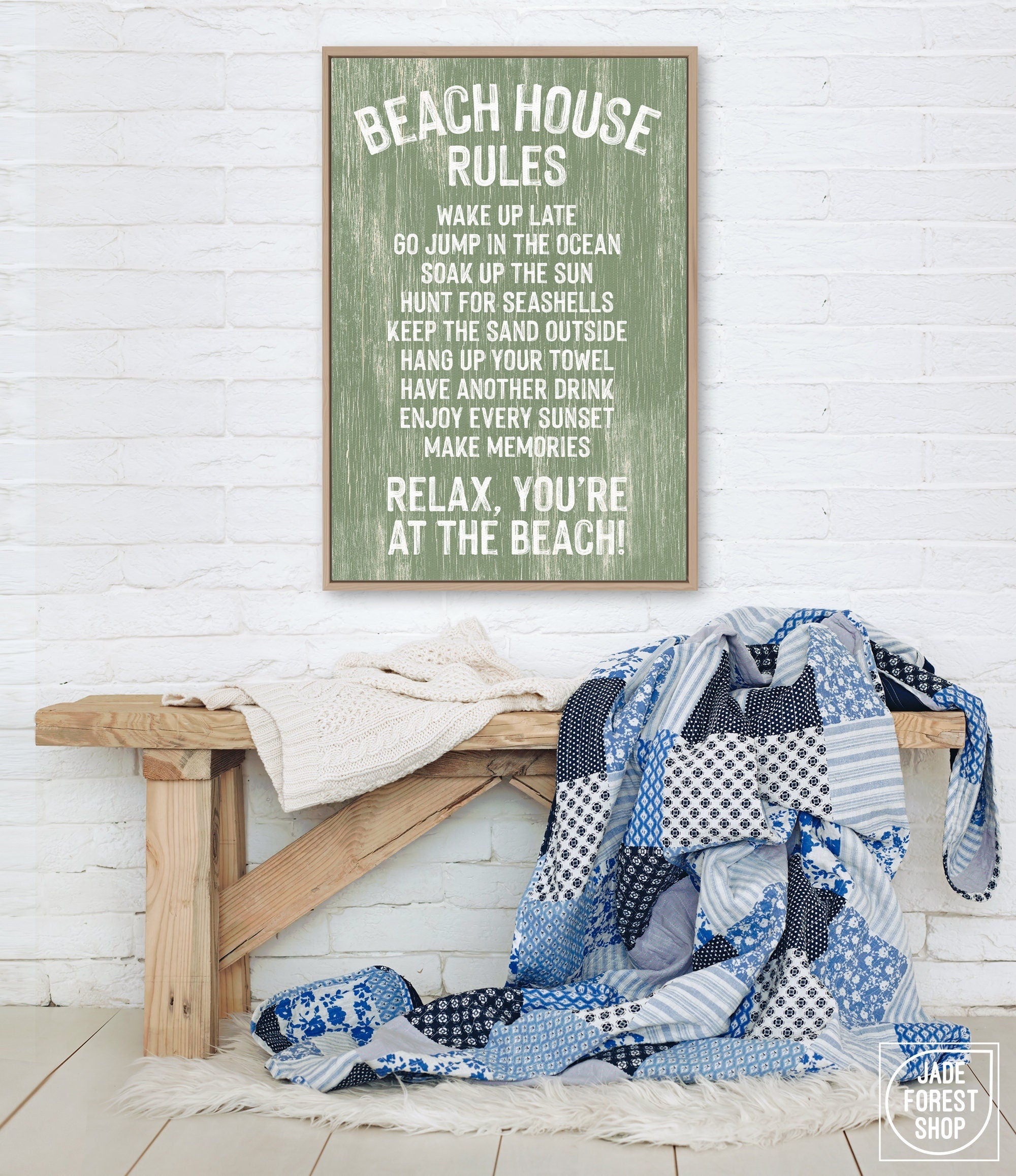 A painted wood Beach House Rules Sign with seagrass hangs above a bench with a blue patchwork quilt, bringing charming coastal wall art to the bright room.