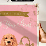a hand holding a framed canvas print with a dog illustration on it. The text on the canvas print reads "Don't forget to wash your paws".
