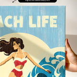 a hand holding a canvas print with a beach scene and a woman in a red swimsuit.