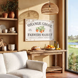 a cozy living room with a rustic wooden table, a white sofa, and a hanging woven light fixture. The table is adorned with various items, including a bowl of fruit, a loaf of bread, and a bottle of olive oil. Above the table, there is a framed sign that reads "Orange Grove Farmers Market Locally Grown Produce".