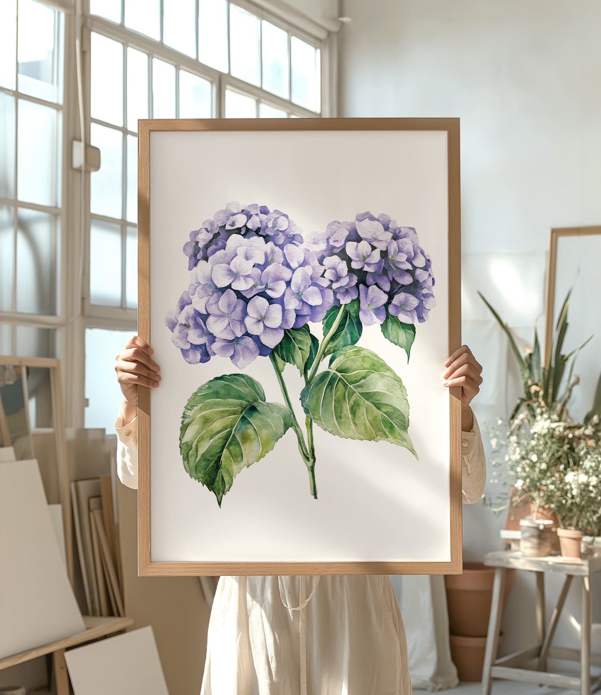A person is holding up a framed painting of purple hydrangea flowers in a room with various potted plants and art supplies.