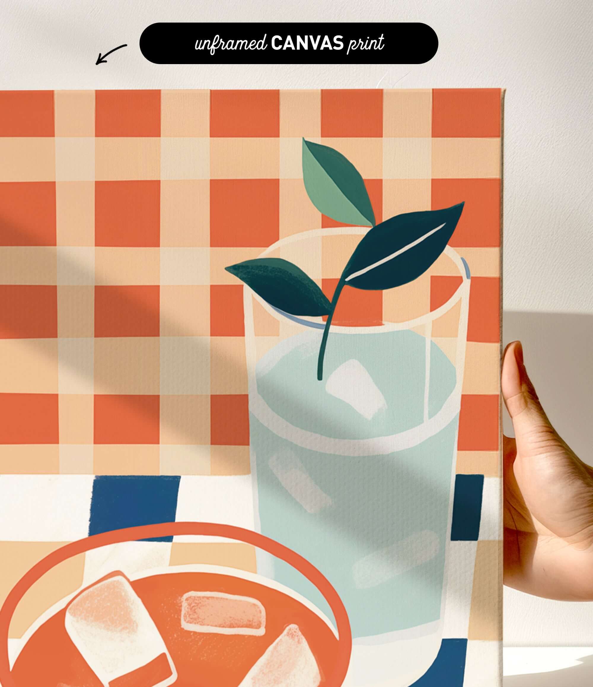 The image is a hand holding a canvas print featuring a glass of water with ice cubes, a plant, and a bowl of food.