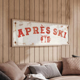 a wooden wall with a framed sign that reads "APRÈS SKI", and there is a couch with pillows in the foreground.