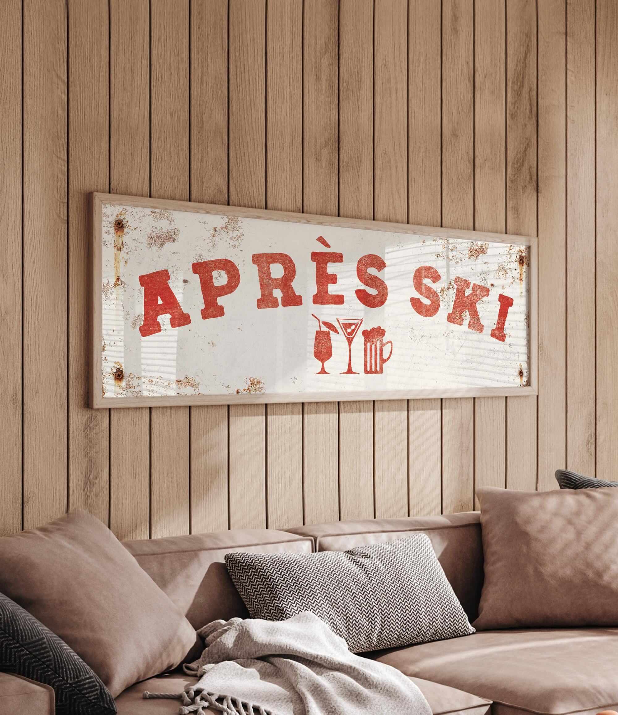 a wooden wall with a framed sign that reads "APRÈS SKI", and there is a couch with pillows in the foreground.