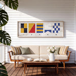 a cozy outdoor seating area with a white sofa, a wooden coffee table, and a framed nautical-themed artwork hanging on the wall above the sofa.