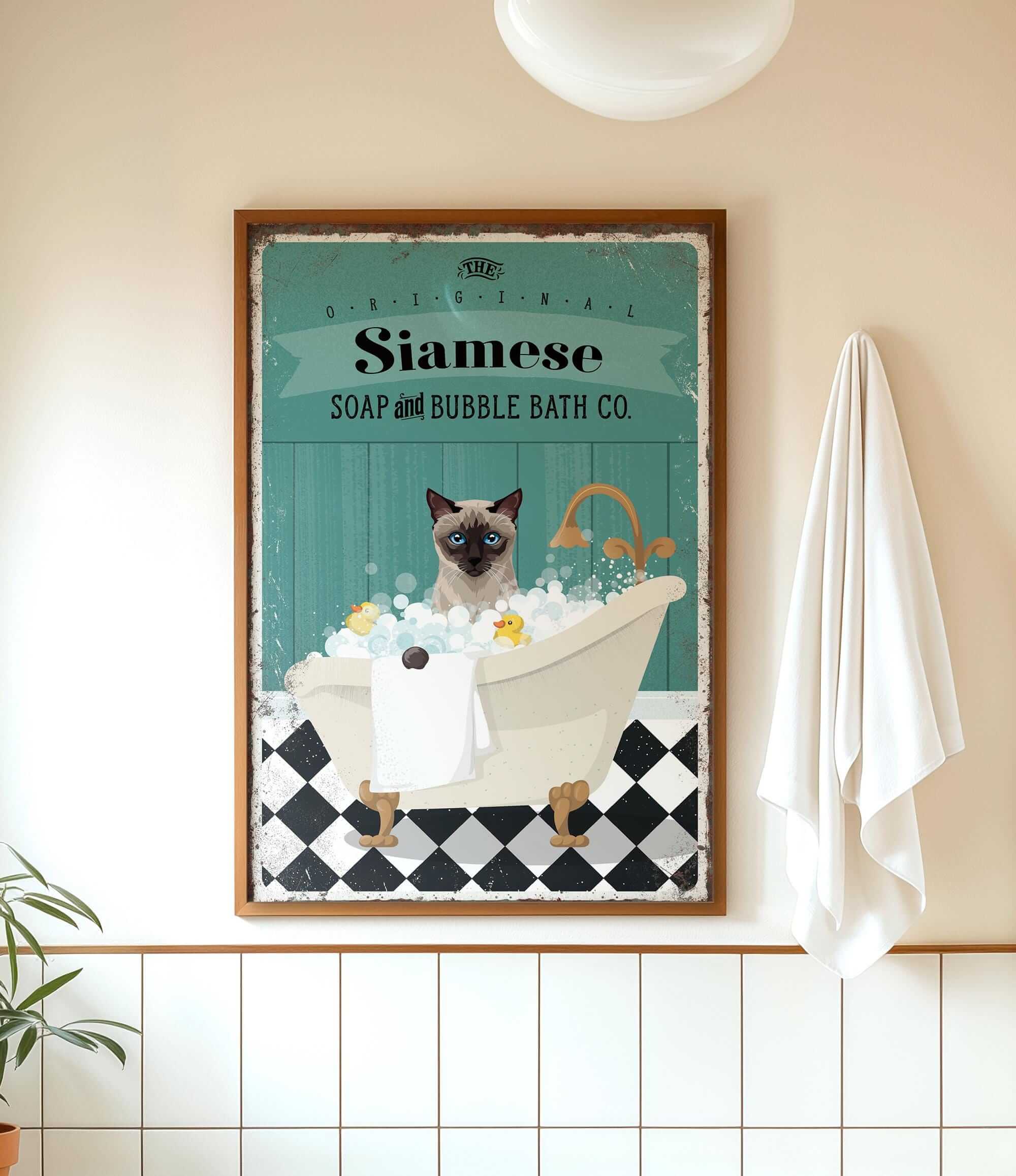 A framed vintage-style poster of a Siamese cat sitting in a bathtub, surrounded by bubbles, with a towel hanging on the wall next to it.