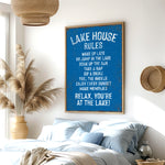 a bedroom with a large blue sign that reads "LAKESHORE RULES" hanging on the wall. The sign lists various lake-related activities and rules, such as "WAKE UP LATE GO JUMP ON THE LAKE COAT UP THE SUN TAKE A NAP FEEL THE BREEZE ENJOY EVERY SUNSET MAKE MEMORIES RELAX YOU'RE AT THE LAKE!" The room has a bed, a potted plant, and a woven basket, creating a cozy and relaxing atmosphere.