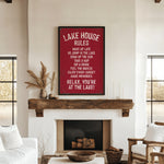 a cozy living room with a fireplace, a wooden mantel, and a framed sign that reads "Lake House Rules" in bold white letters. The sign lists various rules for guests to follow, such as "Wake up late", "Go jump in the lake", "Take a nap", "Sip the sun", "Feel the breeze", "Enjoy every moment", and "Relax, you're at the lake!" The room also includes a couch, a chair, and a potted plant, creating a warm and inviting atmosphere.