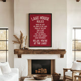 a cozy living room with a fireplace, a wooden mantel, and a framed sign that reads "Lake House Rules" in bold white letters. The sign lists various rules for guests to follow, such as "Wake up late", "Go jump in the lake", "Take a nap", "Sip the sun", "Feel the breeze", "Enjoy every moment", and "Relax, you're at the lake!" The room also includes a couch, a chair, and a potted plant, creating a warm and inviting atmosphere.