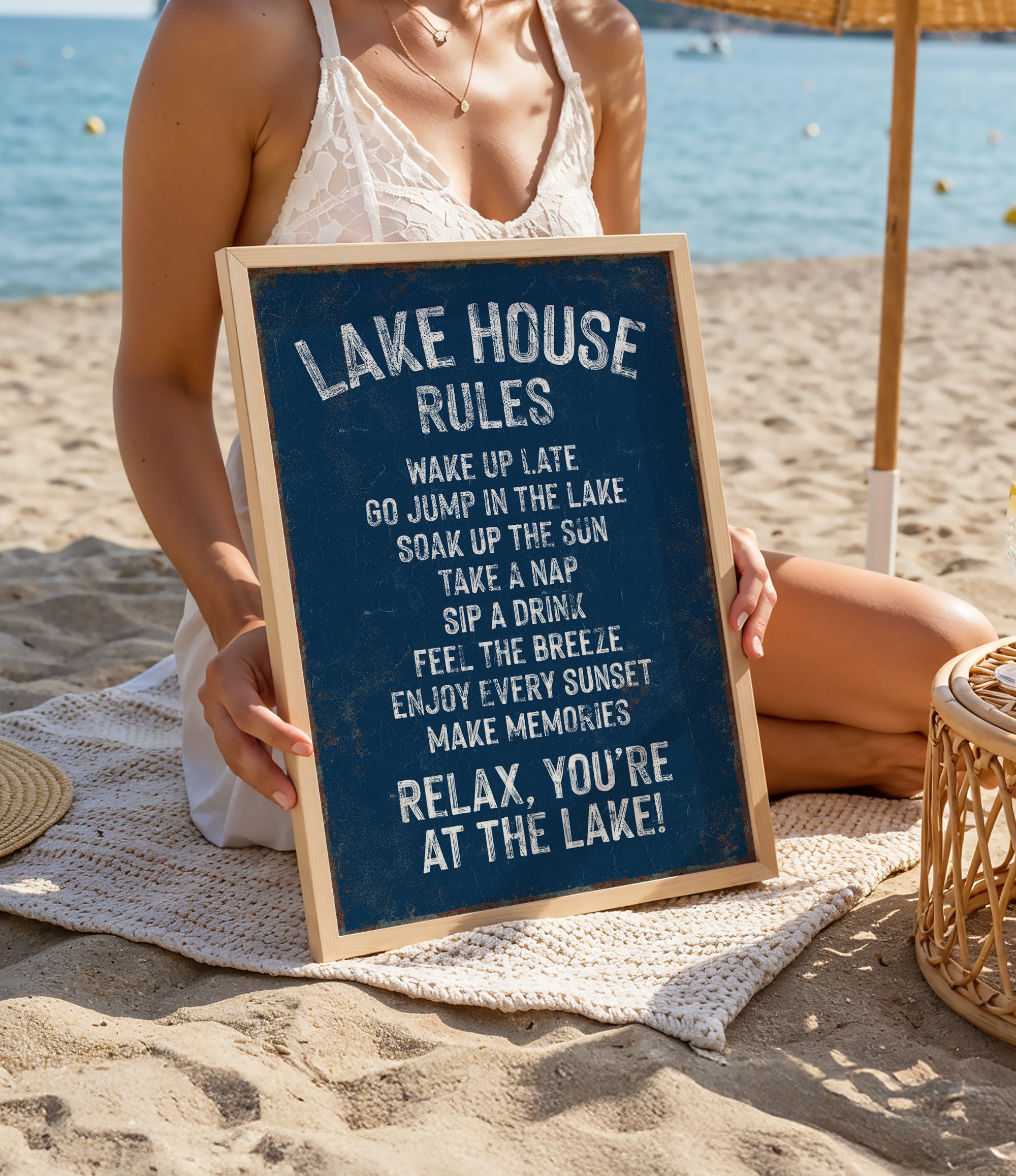 A woman is sitting on a beach holding a sign with rules for the lake house.