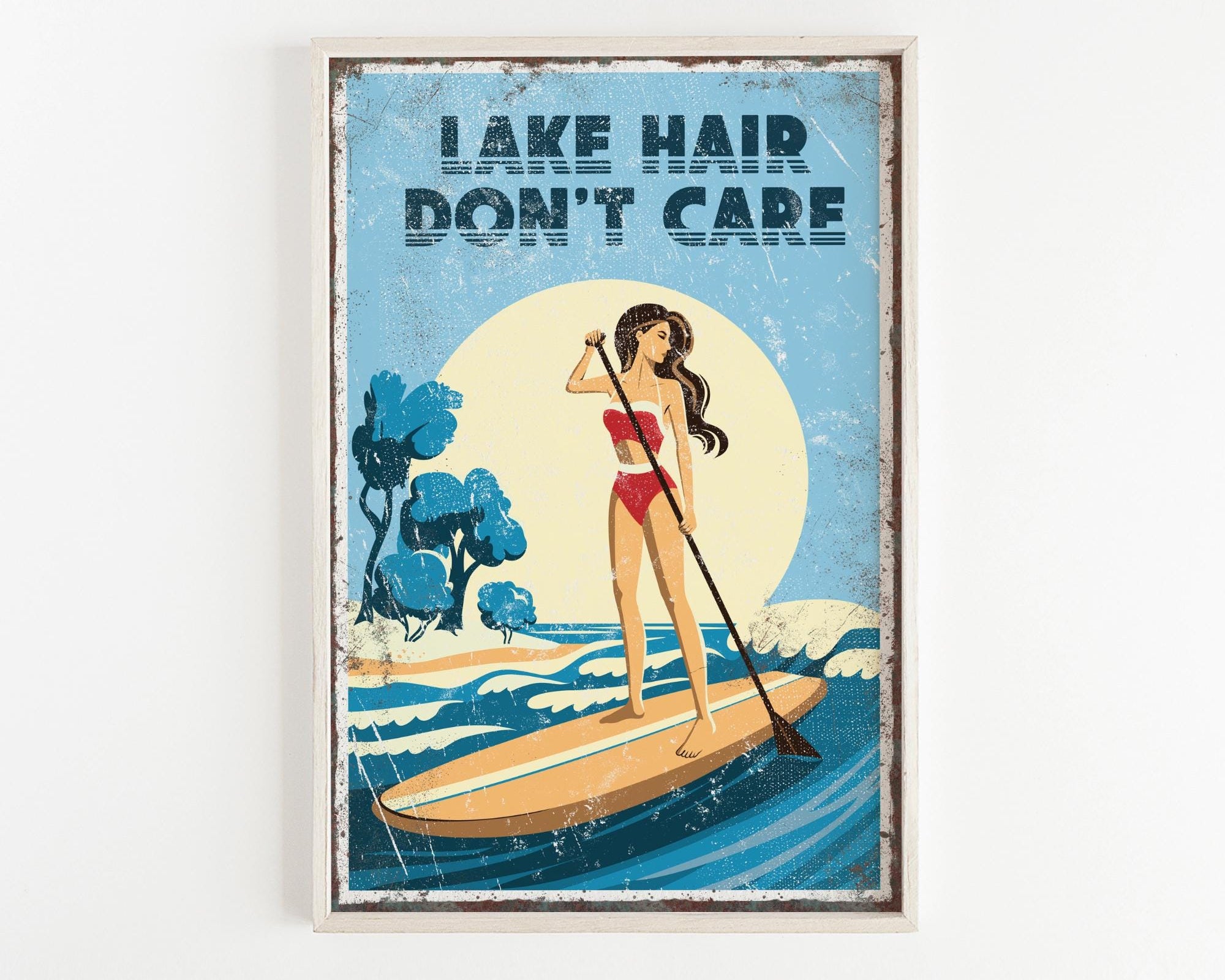 A framed poster with a woman paddleboarding on a lake, with the text "LAKESHAIR DON'T CARE" written above her.