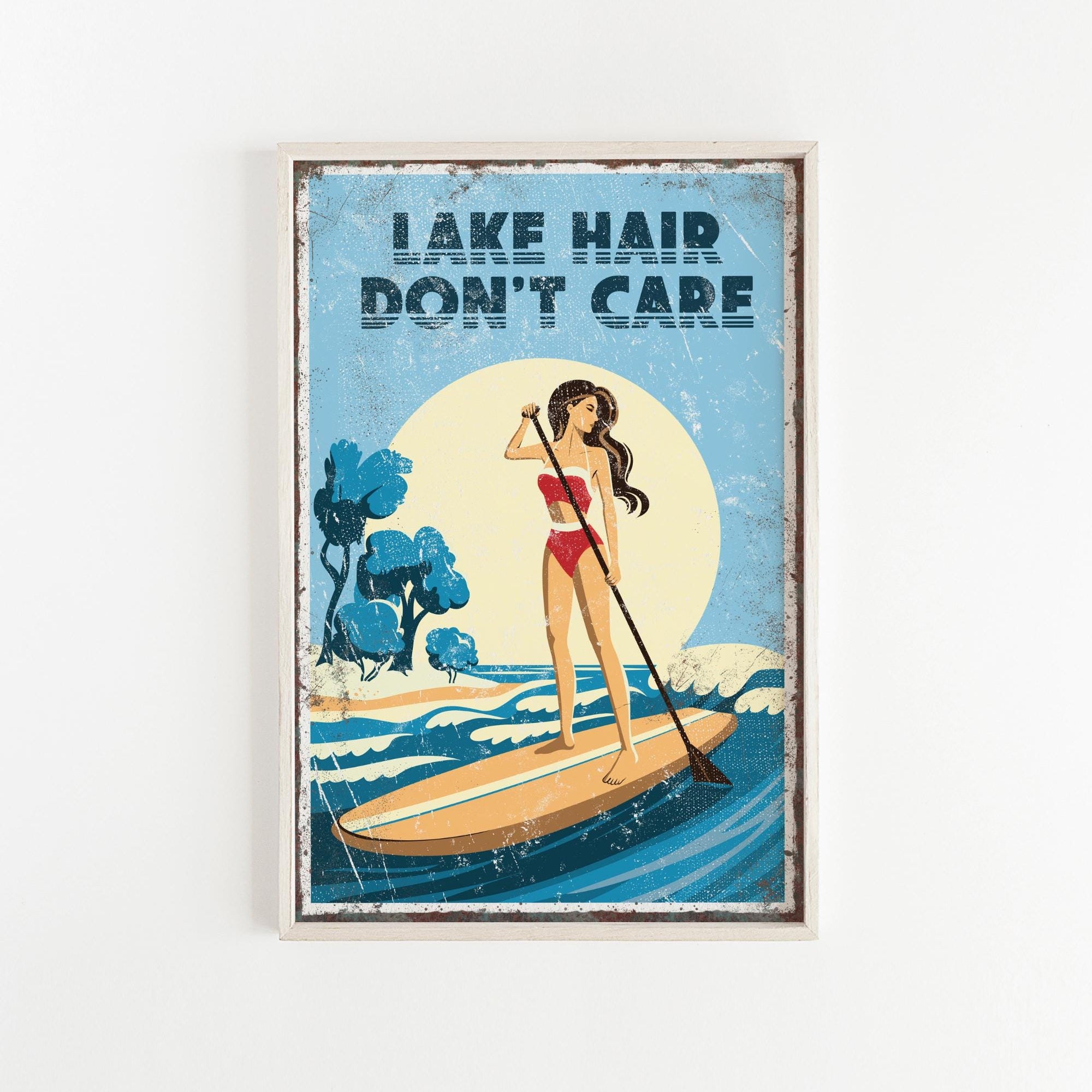 A framed poster with a woman paddleboarding on a lake, with the text "LAKESHAIR DON'T CARE" written above her.