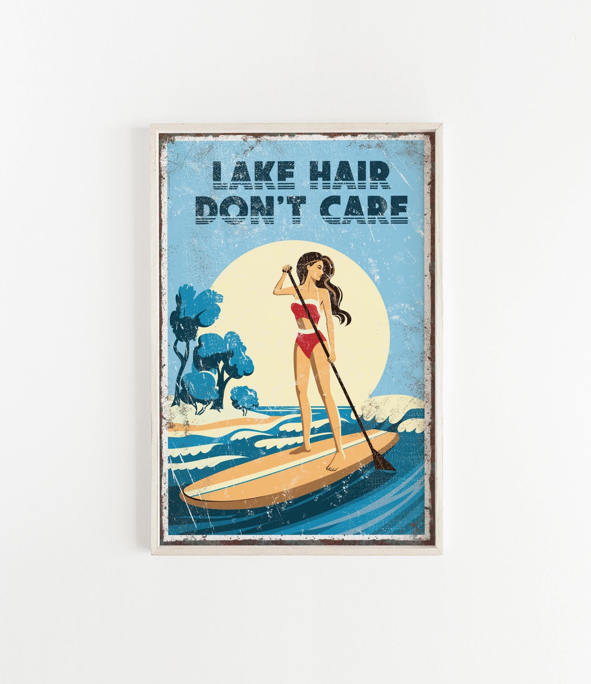 A framed poster with a woman paddleboarding on a lake, with the text "LAKESHAIR DON'T CARE" written above her.