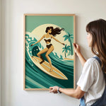 A woman is standing in front of a framed illustration of a woman surfing on a wave, wearing a bikini.