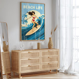 a framed poster of a woman surfing on a wave, with the text "BEACH LIFE" written above it. The poster is displayed on a wall above a wooden dresser with drawers.