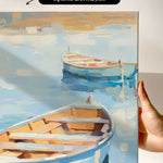 a hand holding a framed painting of two boats on a body of water.