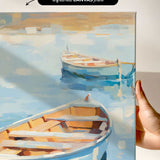 a hand holding a framed painting of two boats on a body of water.