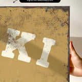 a hand holding a piece of artwork with a distressed, aged appearance. The artwork has a yellowish-brown background with splatters and a distressed texture, giving it a vintage or aged look.