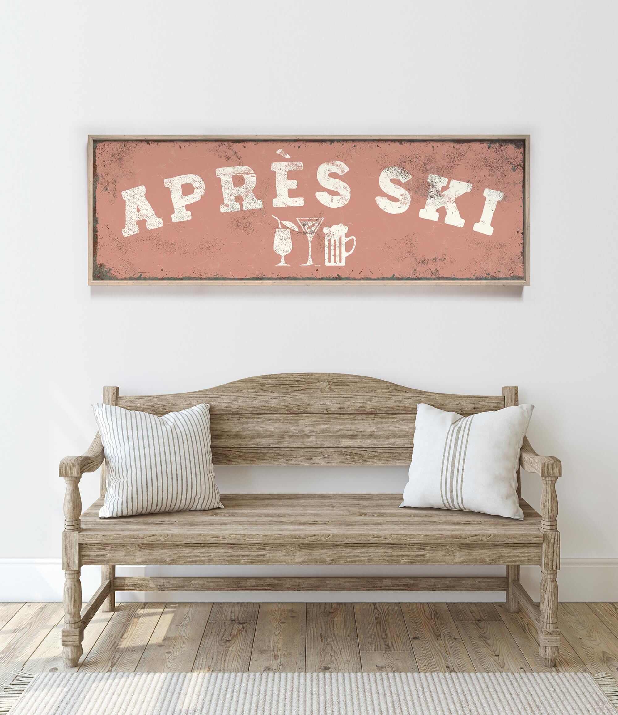 a rustic wooden bench with two striped pillows, set against a white wall with a framed sign above it that reads "APRES SKI".