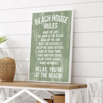 The Beach House Rules Sign, Painted Wood, Seagrass, with white text on green, sits on a wooden table in a coastal-themed room—perfect beach house wall decor.