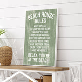 The Beach House Rules Sign, Painted Wood, Seagrass, with white text on green, sits on a wooden table in a coastal-themed room—perfect beach house wall decor.