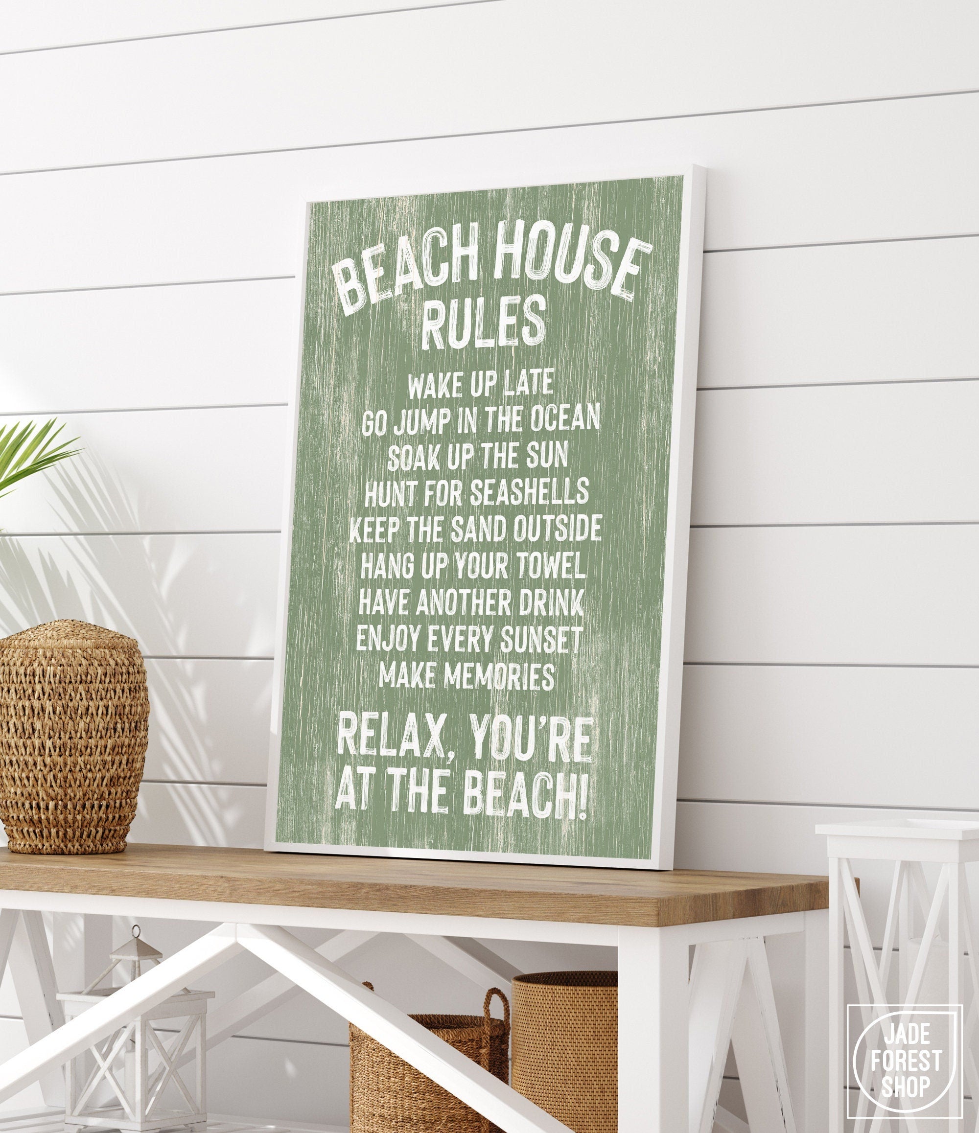 The Beach House Rules Sign, Painted Wood, Seagrass, with white text on green, sits on a wooden table in a coastal-themed room—perfect beach house wall decor.