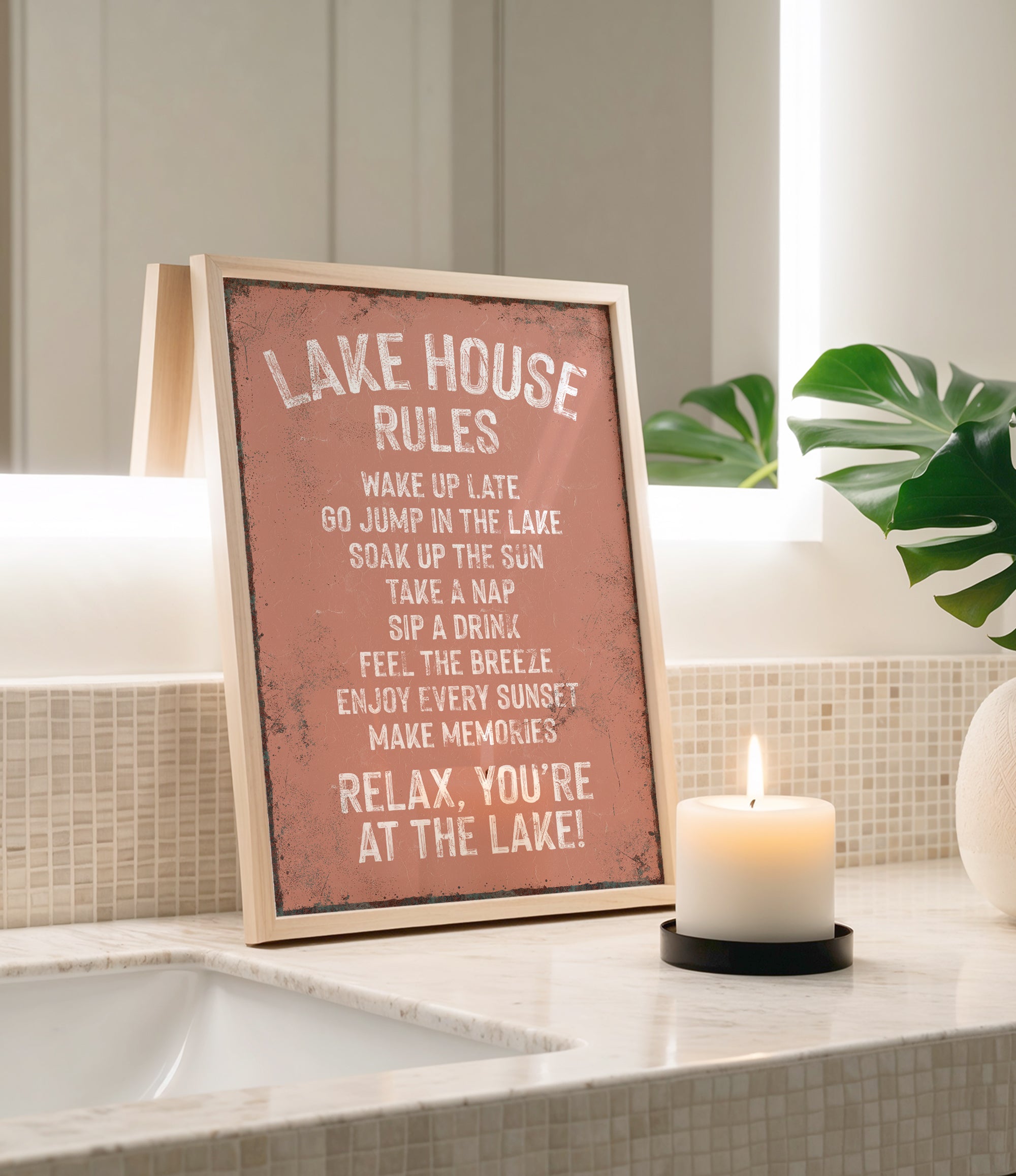 a framed sign on a bathroom counter with a lit candle in front of it, creating a relaxing atmosphere.