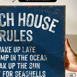 a hand holding a sign that says beach house rules