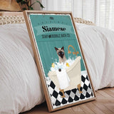 A framed poster depicting a Siamese cat sitting in a bathtub filled with bubbles, with a towel and a sink nearby.
